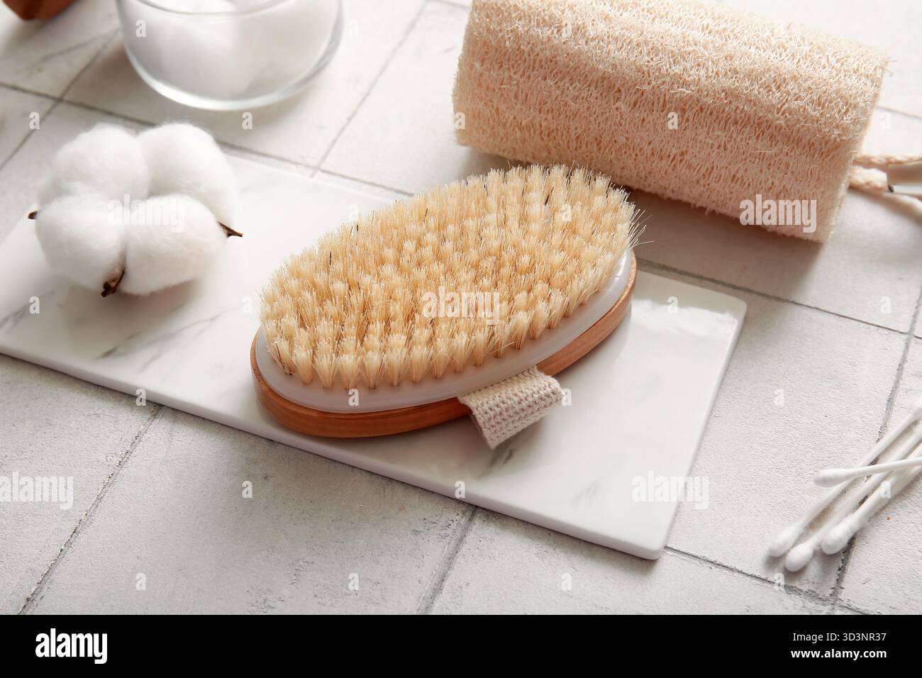 Spazzola massaggiante con bastoncini di cotone, loofah e fiore su sfondo piastrellato bianco, primo piano Foto Stock