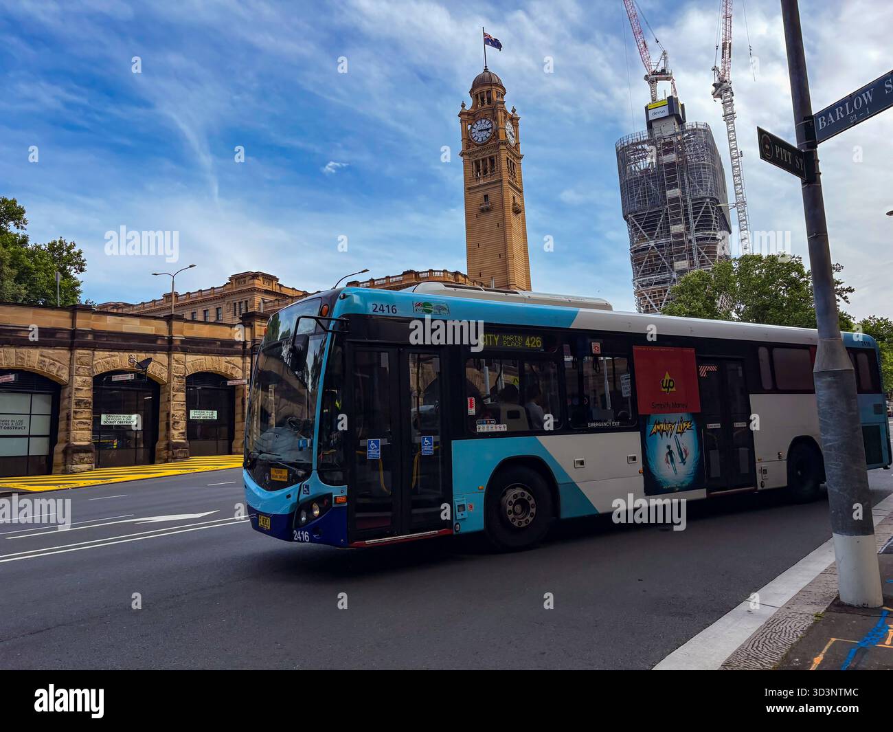 La Torre dell'orologio della stazione centrale di Sydney si erge in alto dietro un autobus pubblico che guida su una strada della città. Questa immagine cattura i trasporti pubblici urbani e l'arco iconico Foto Stock