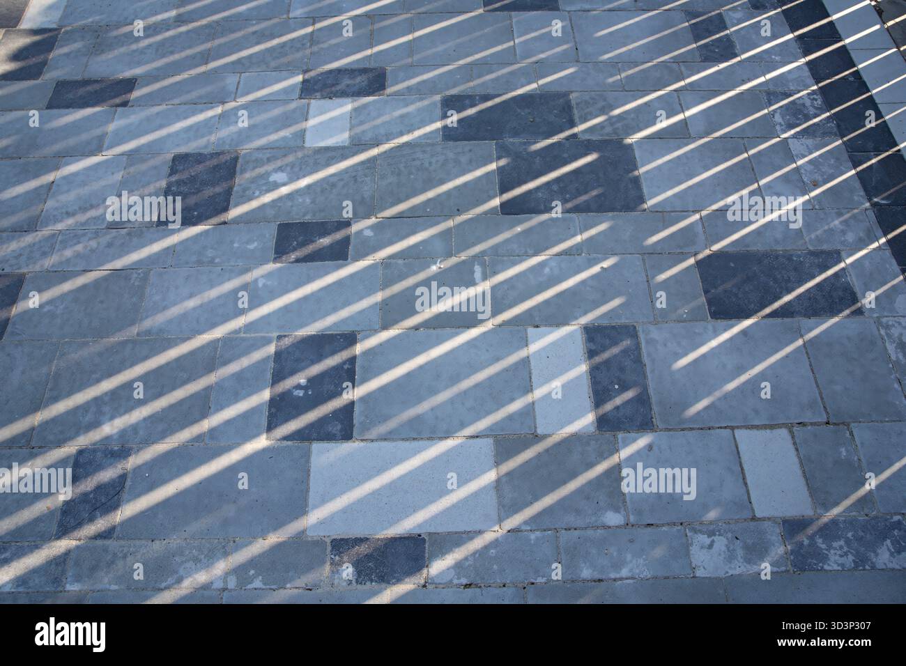 Pavimentazione geometrica in pietra con lunghe ombre diagonali che creano un motivo astratto Foto Stock