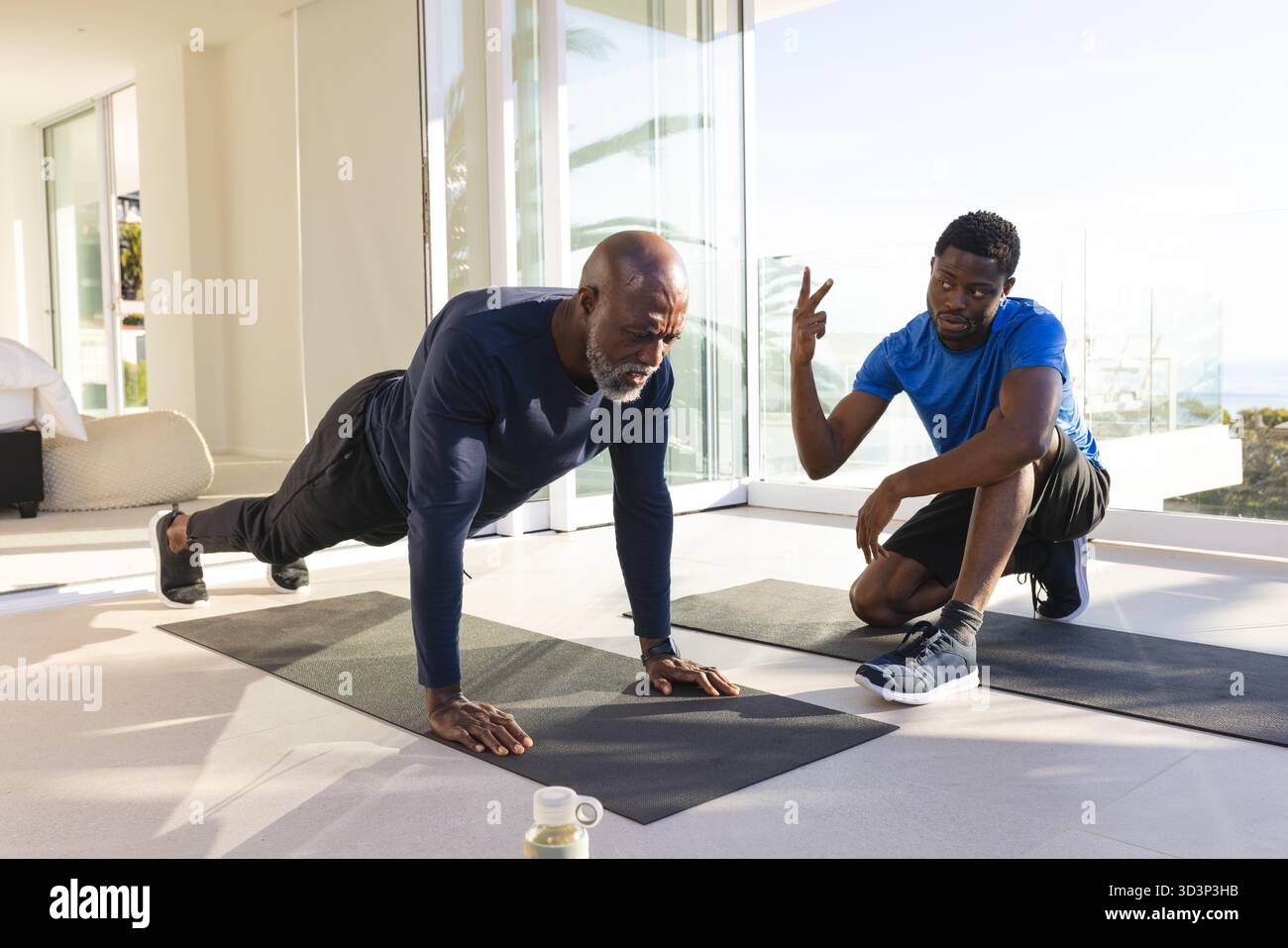 Con una bottiglia d'acqua, tiene in salotto un addestratore afroamericano e un cliente afroamericano in posa alta Foto Stock