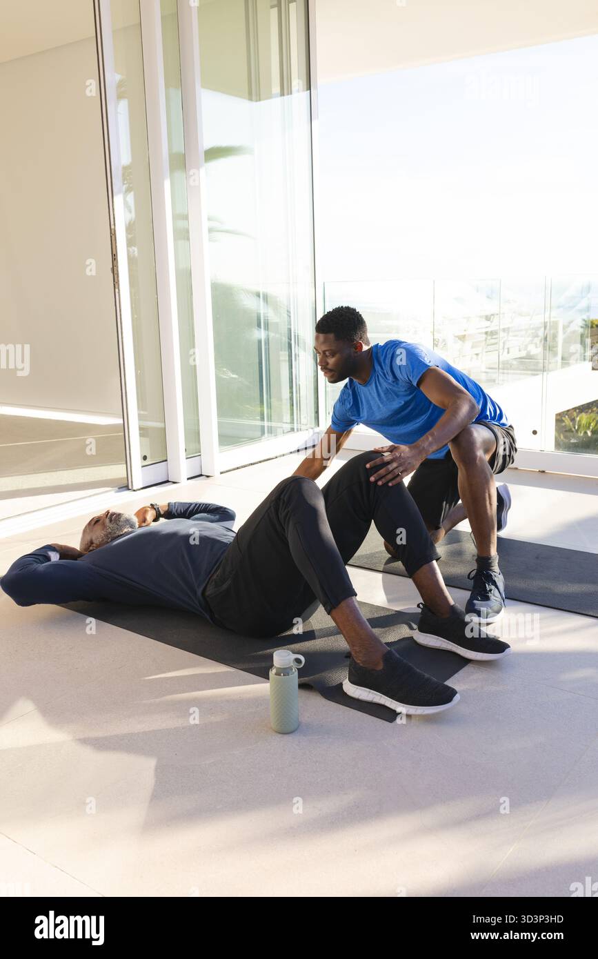 Preparatore afroamericano e cliente che lavora nella palestra domestica, con porte in vetro e tappetini Foto Stock