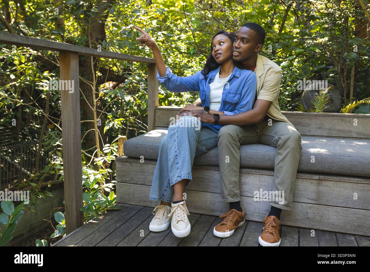 Punta la coppia afroamericana seduta su una panchina di legno sul ponte, abbracciando sotto la luce del sole Foto Stock