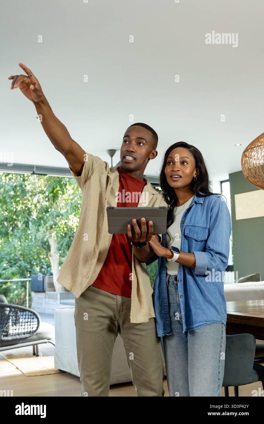 Puntando una coppia afroamericana che pianifica la disposizione della stanza in un'area soggiorno aperta, con tablet Foto Stock