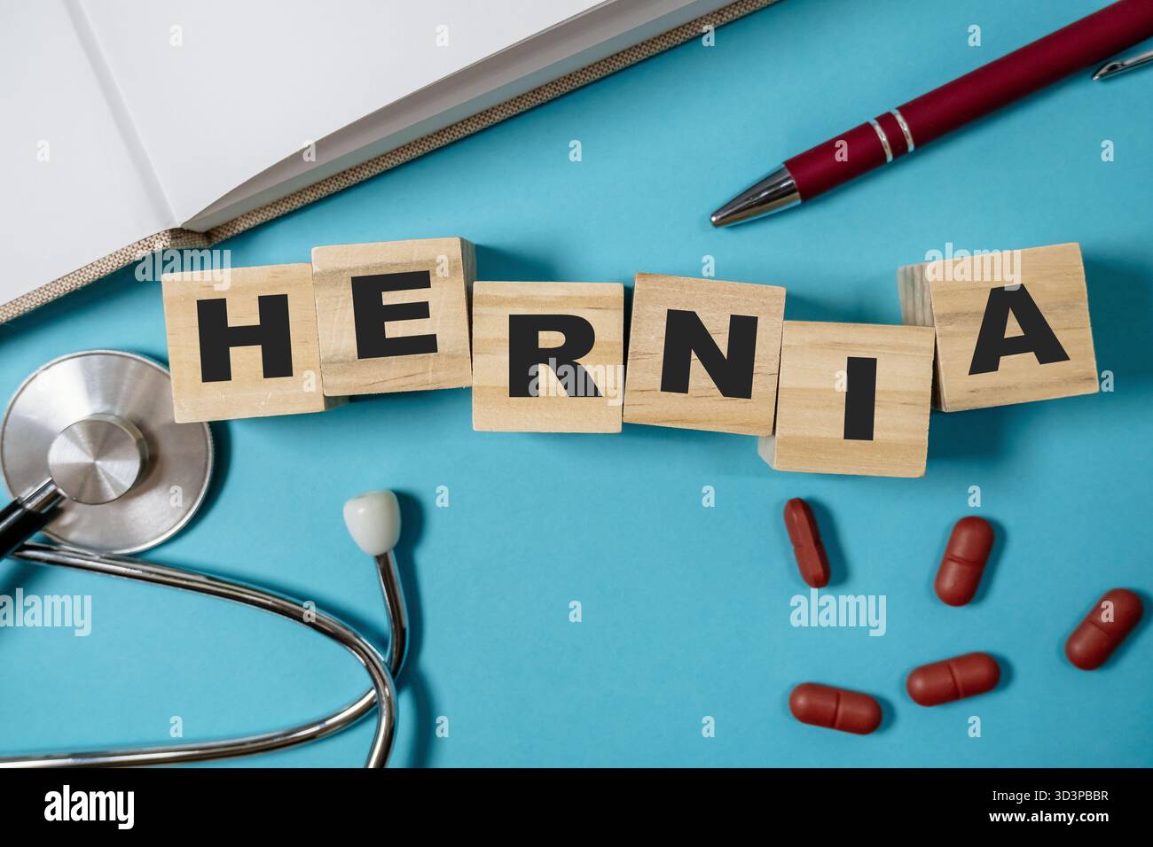 Blocco di legno con la parola ERNIA scritta su di esso. Il blocco si trova sopra una superficie blu con una penna e uno stetoscopio Foto Stock