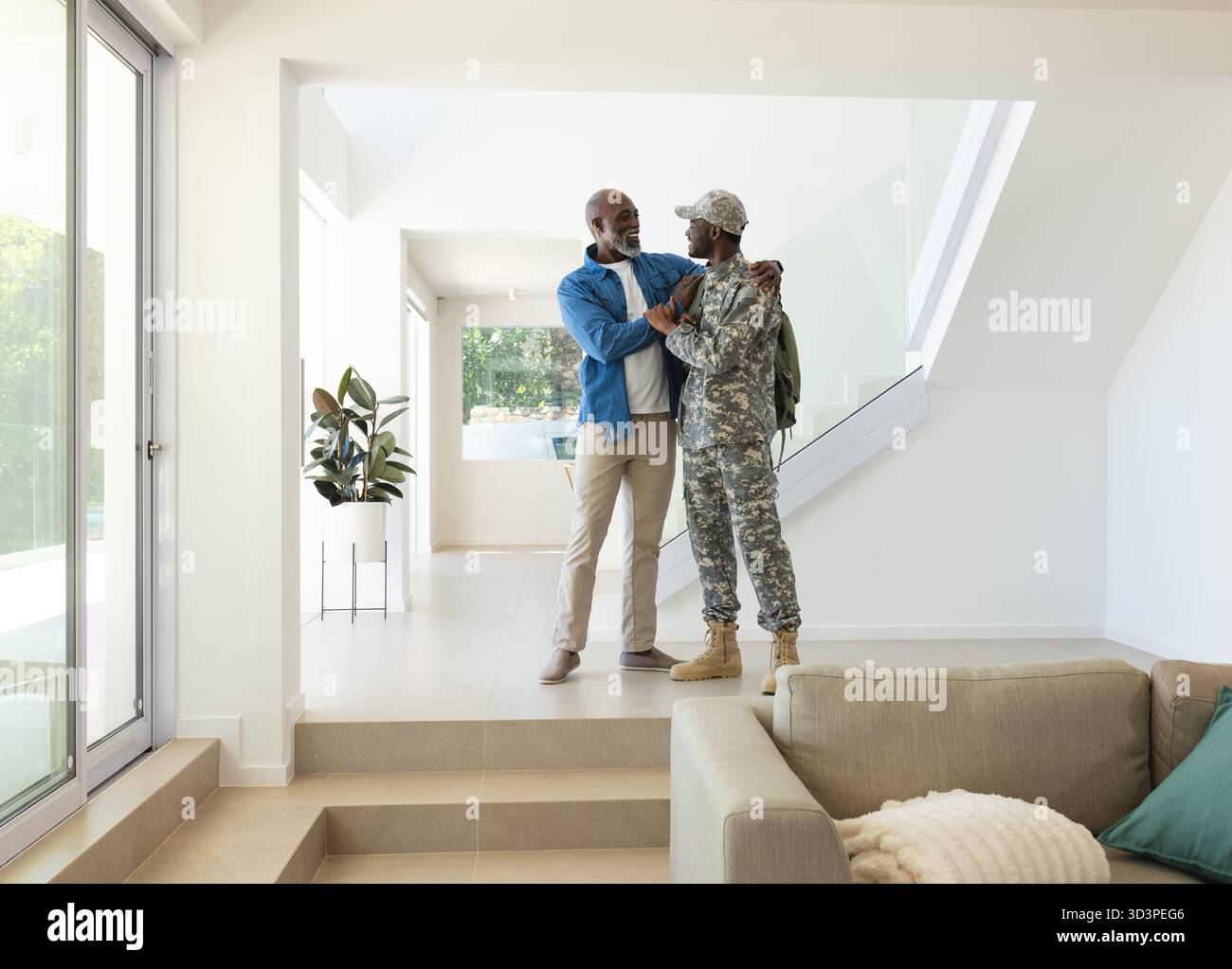 Abbracciare padre e figlio afroamericani che condividono l'abbraccio all'ingresso, con zaino militare e pianta Foto Stock