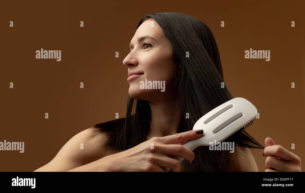 Donna che pulisce capelli lunghi e lisci con una spazzola bianca che sorride con calma Foto Stock