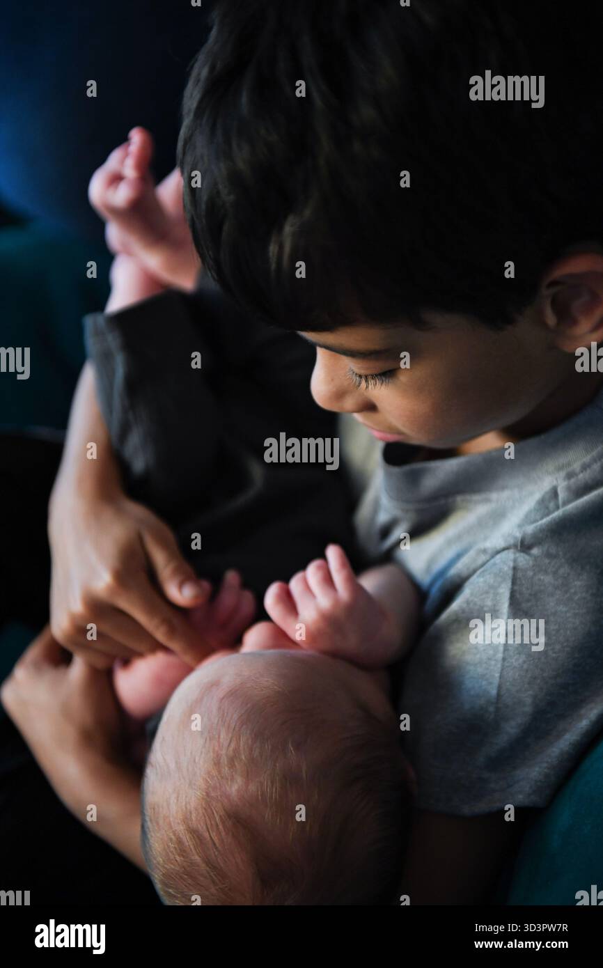 Il bambino più grande tiene e guarda delicatamente il neonato in braccio Foto Stock