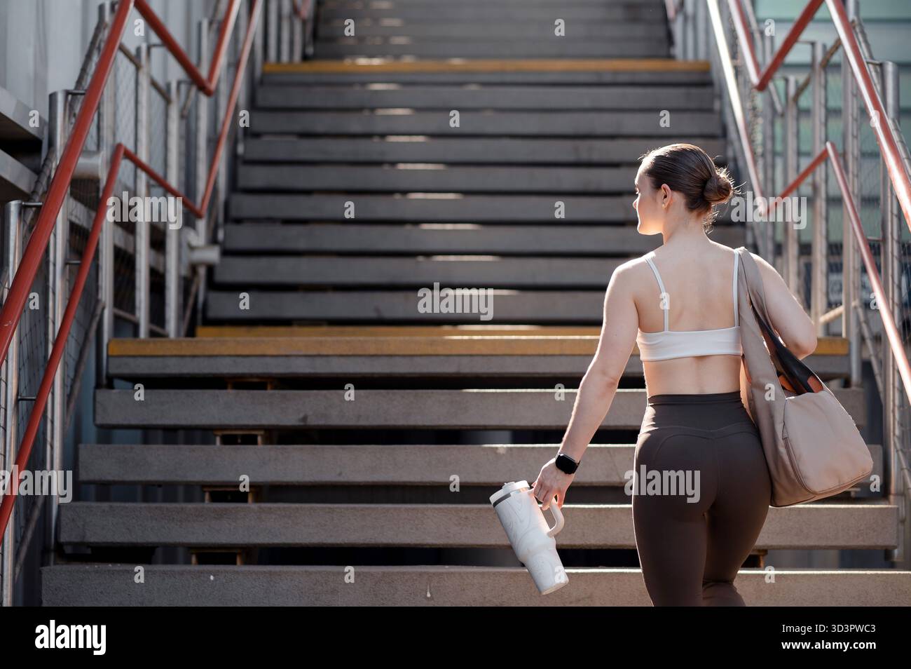 Donna che sale le scale con una bottiglia d'acqua e una borsa Foto Stock