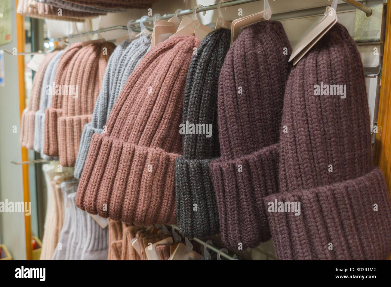 Una varietà di comodi cappelli invernali lavorati a maglia sono esposti ordinatamente sugli scaffali dei negozi. I cappelli sono disponibili in diversi colori, tra cui rosa, grigio e viola, perfetto Foto Stock