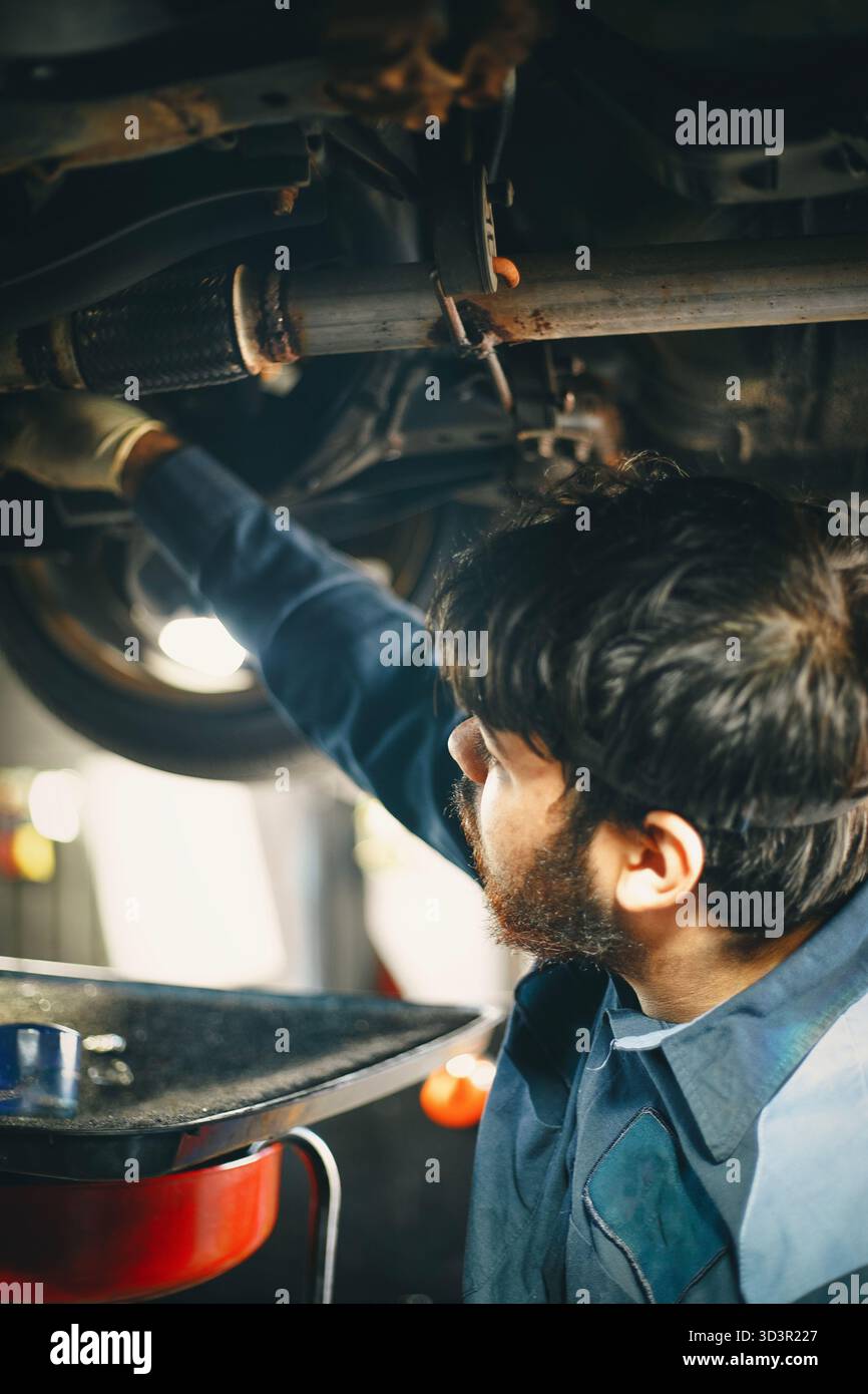 Un meccanico è incentrato sull'esame della parte inferiore di un veicolo. Foto Stock