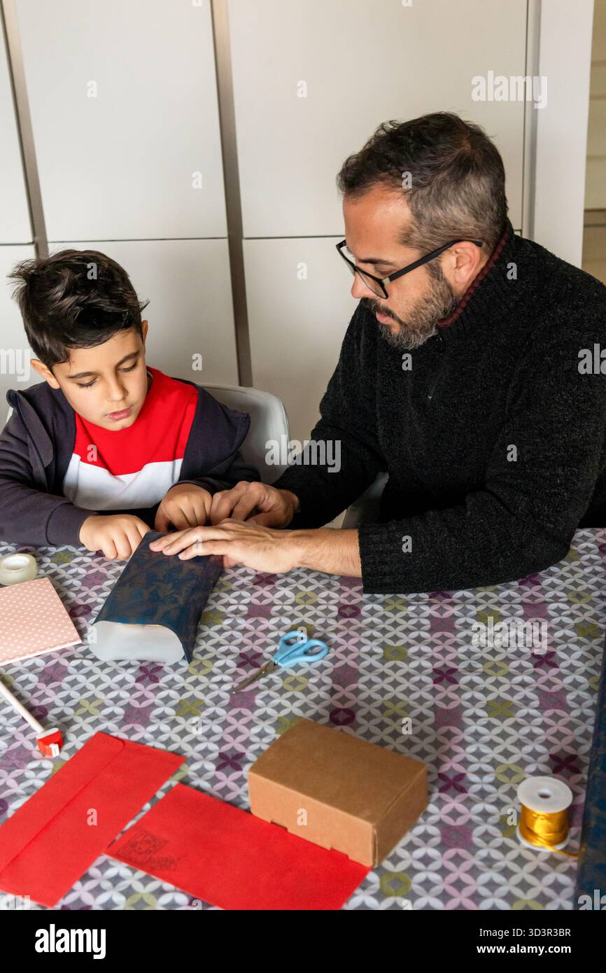 Un padre guida il bambino a portare a casa un regalo di Natale, circondato da provviste natalizie. La scena cattura la gioia e il legame della preparazione delle vacanze Foto Stock