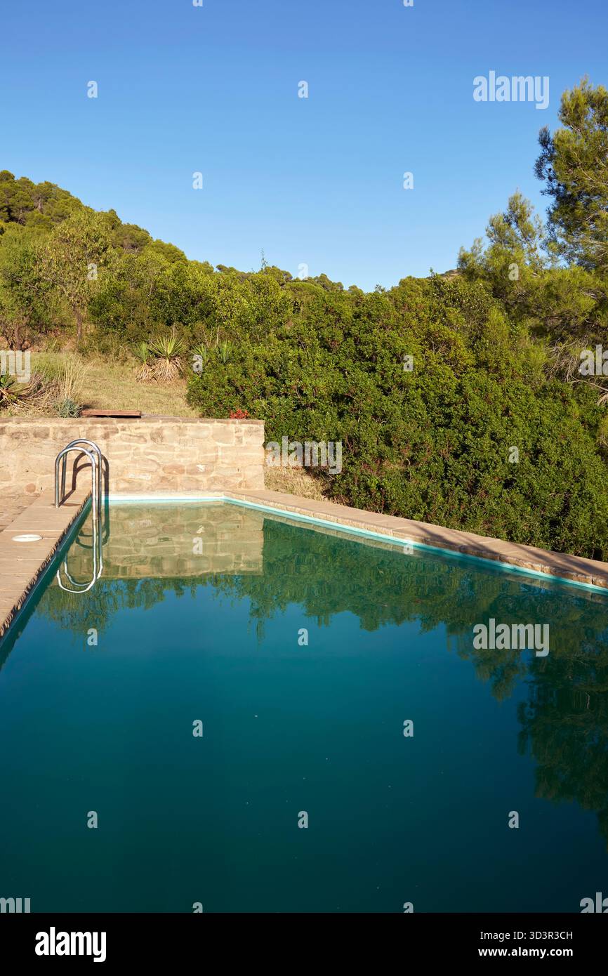 Una tranquilla piscina all'aperto è circondata da vegetazione lussureggiante e alberi, offrendo un tranquillo rifugio nella campagna di Mura, situata a Bages, Cat Foto Stock