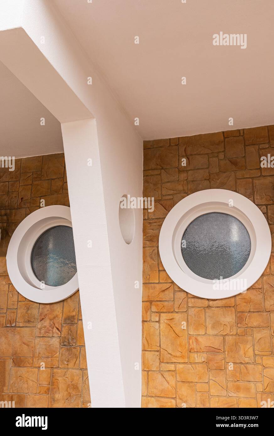 Vista ravvicinata dell'esterno di una casa moderna con finestre circolari poste su muri in pietra testurizzata, che mettono in risalto elementi architettonici unici Foto Stock