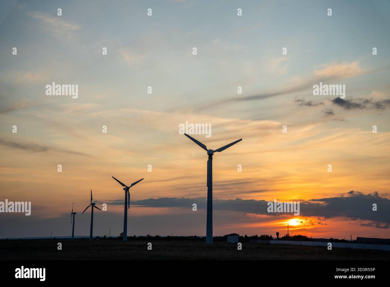 Le turbine eoliche si stagliano in alto contro un vibrante cielo al tramonto, evidenziando la transizione verso l'energia verde. Il tranquillo paesaggio cattura l'essenza di susta Foto Stock