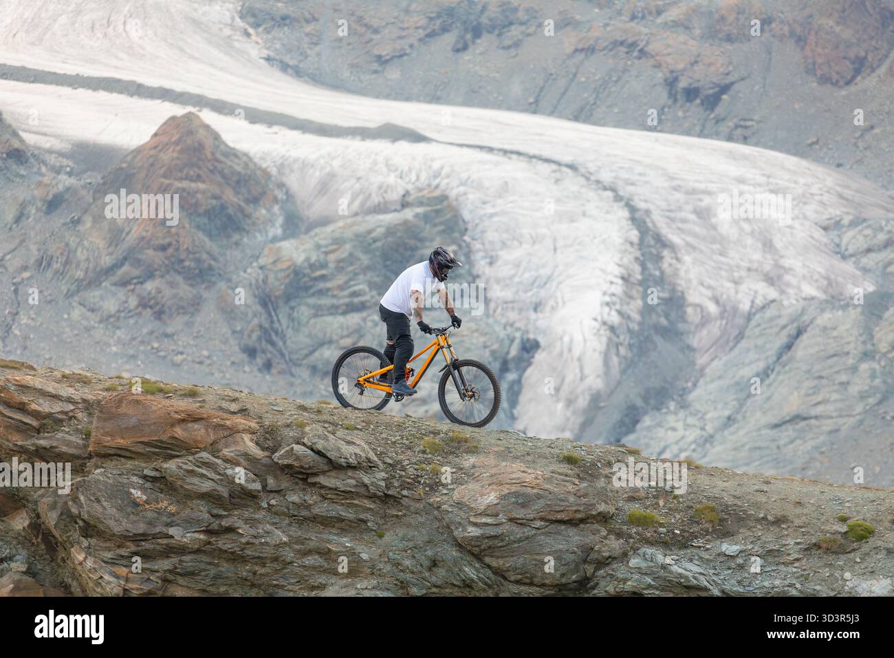 Un mountain bike percorre un impegnativo sentiero roccioso contro un maestoso sfondo alpino svizzero vicino a Zermatt. Prova l'adrenalina e la bellezza panoramica Foto Stock
