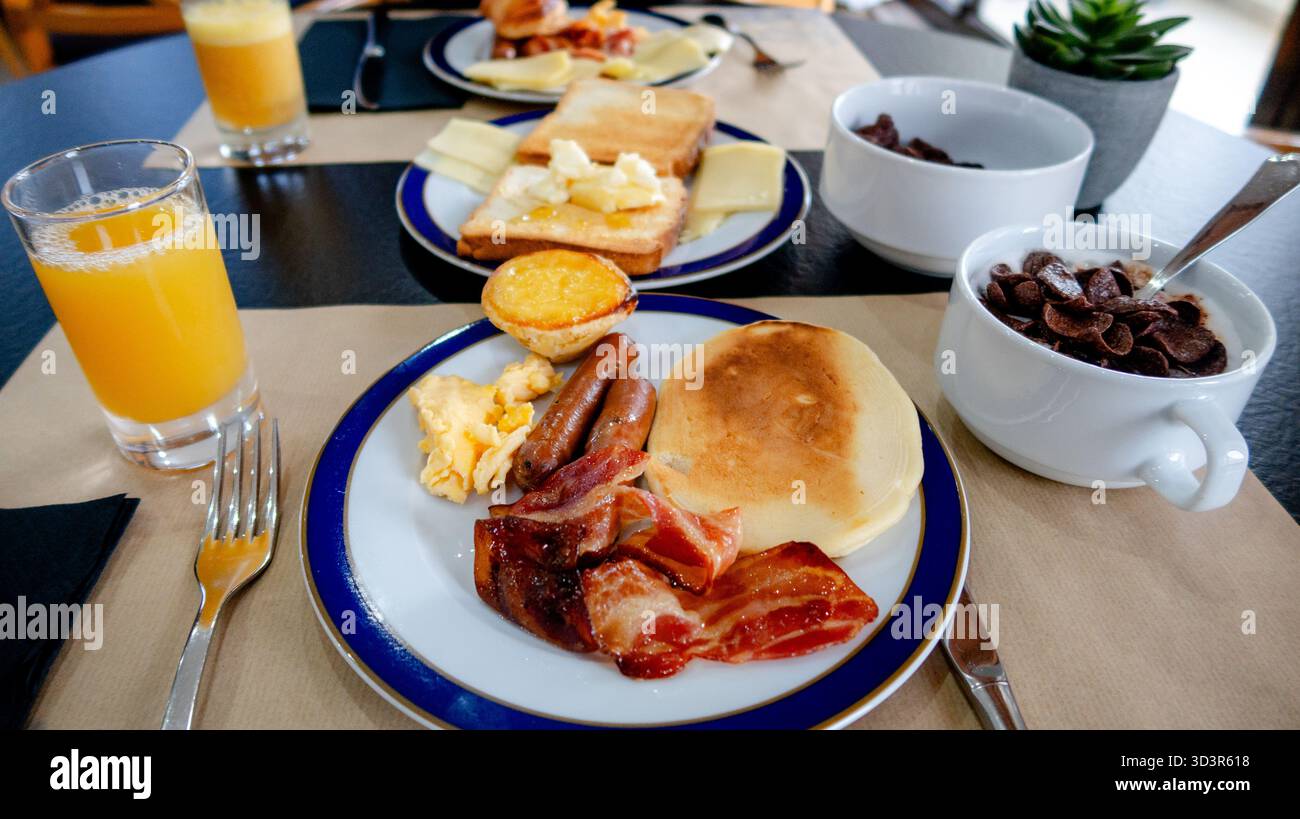 Una ricca colazione con pancetta croccante, salsicce, uova strapazzate, pancake, pane tostato con formaggio e miele locali, cereali, pasteis de nata e fresco Foto Stock