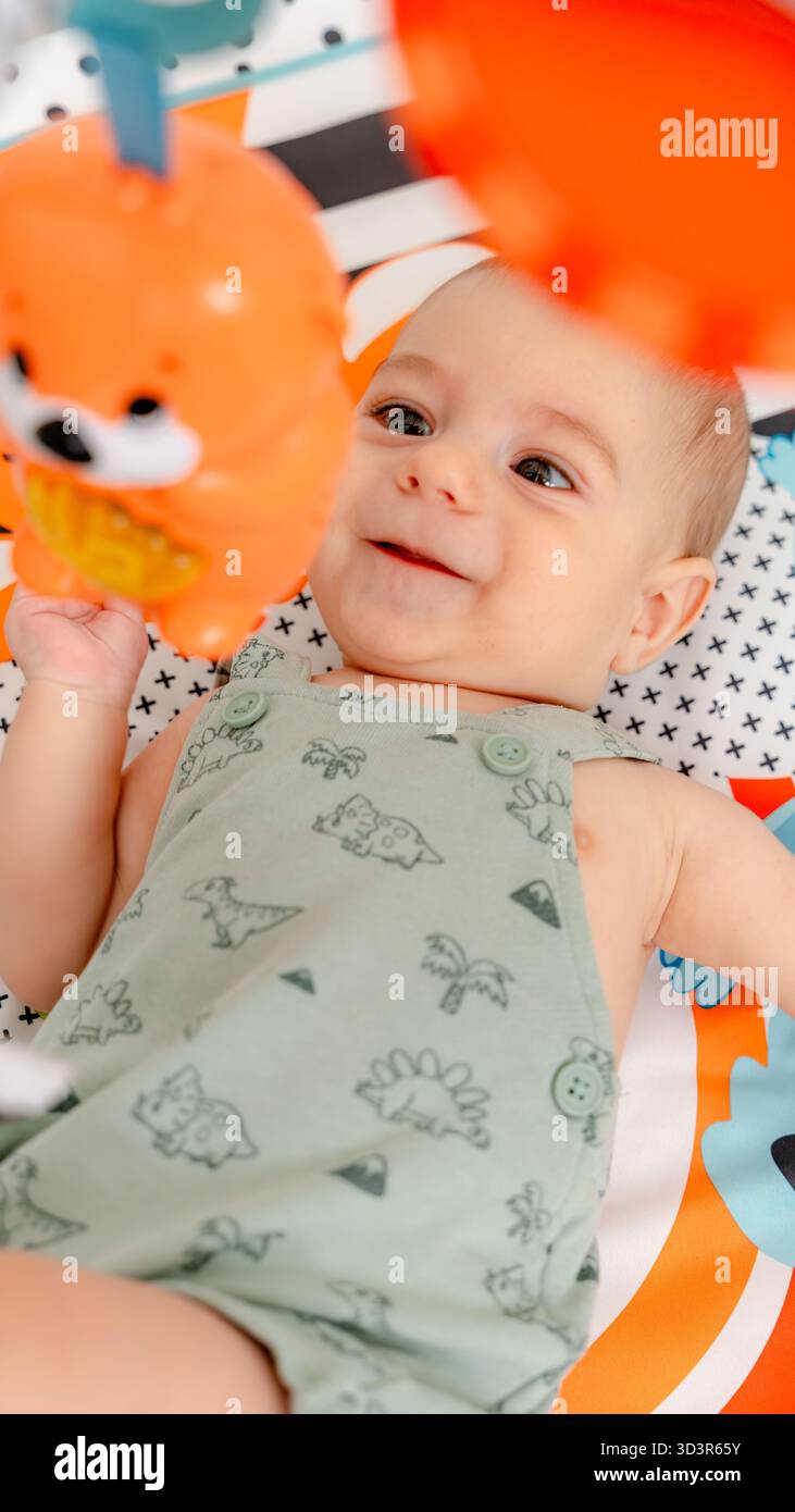 Un bambino felice in un simpatico costume da dinosauro è impegnato con un giocattolo su un tappeto colorato per attività. Questo cattura un momento gioioso di apprendimento e sviluppo precoce Foto Stock