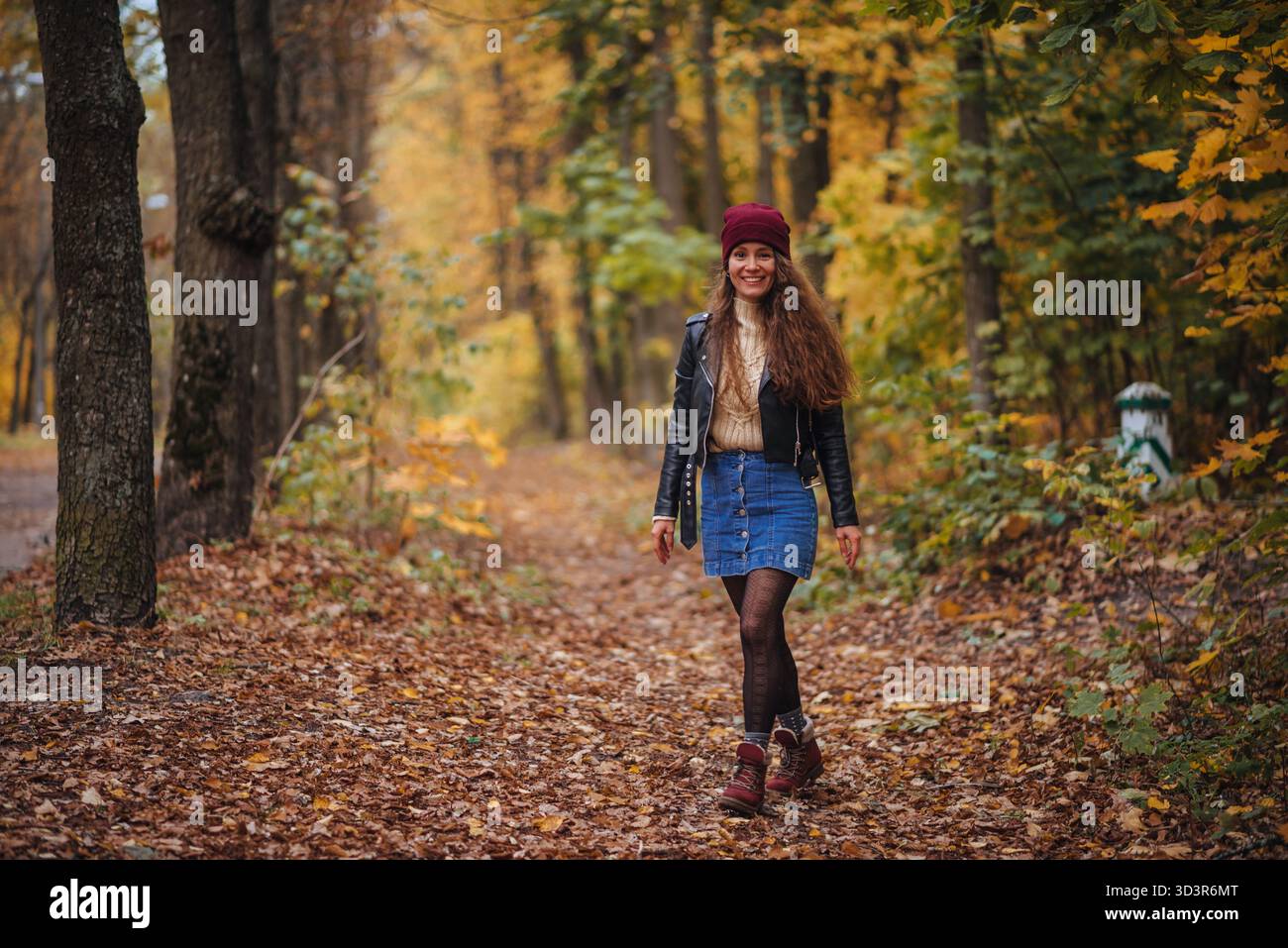 Una donna allegra in abito autunnale cammina attraverso un parco colorato coperto di foglie cadute. La scena cattura l'essenza della felicità e della tranquillità Foto Stock