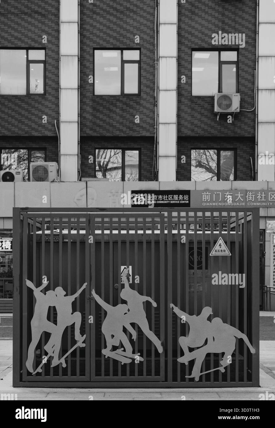 Vista in bianco e nero di un edificio a Pechino con un cancello decorato da silhouette metalliche di skateboard Foto Stock
