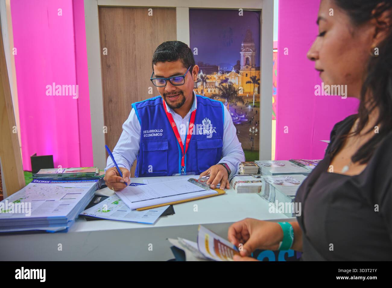 Lima, perù. 01 novembre 2025: funzionario maschile che registra una visitatrice femminile presso un banco informazioni eventi a lima, perù Foto Stock