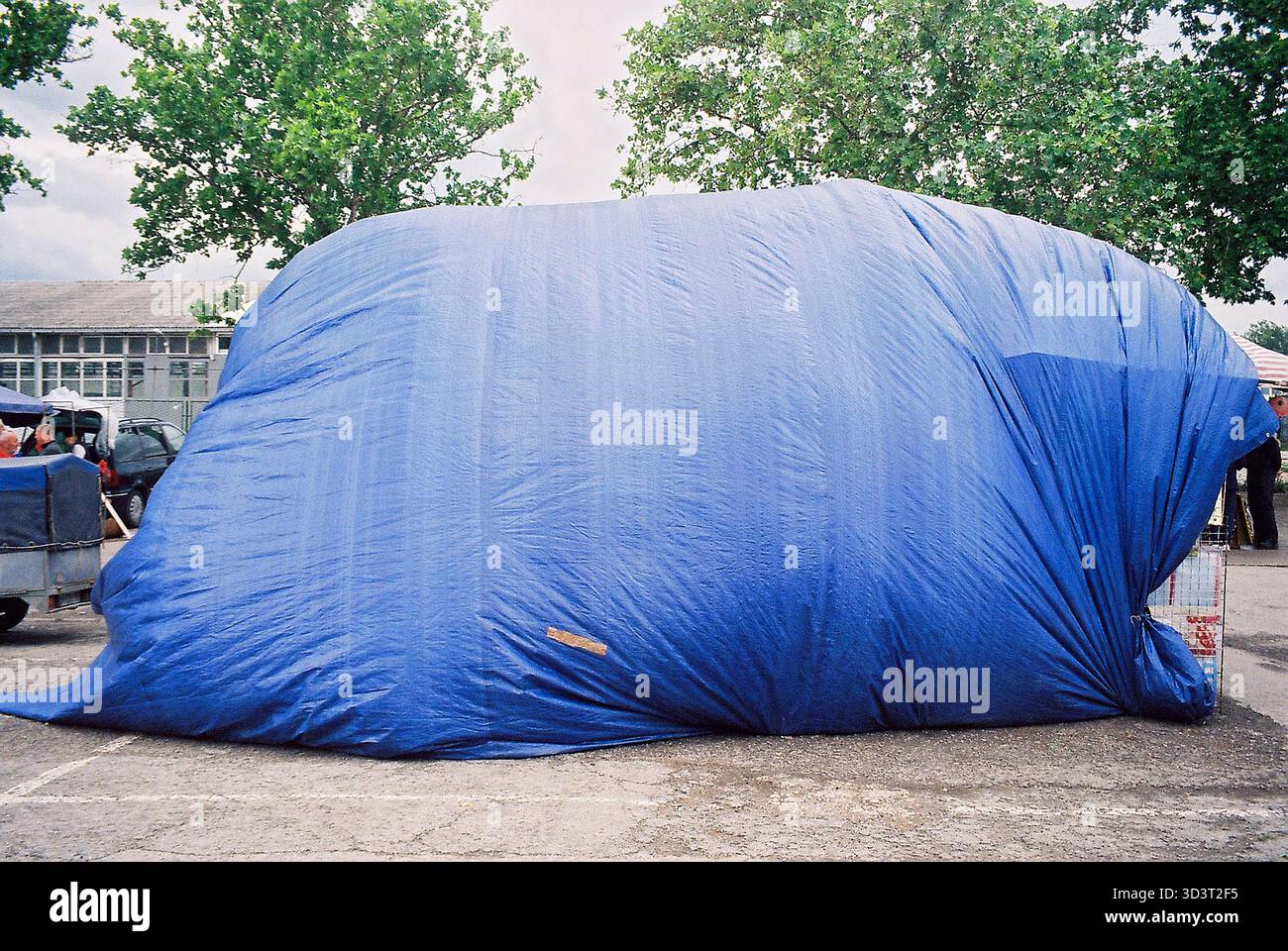Il vento gonfia un telo blu del mercato come una mongolfiera gigante sopra una stalla, catturato in luce analogica, sottolineando il movimento e il caos quotidiano. Foto Stock