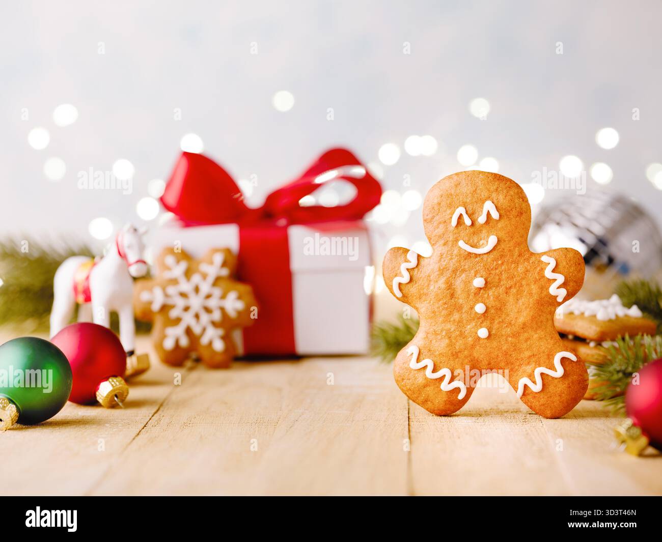 Biscotti di pan di zenzero natalizio con decorazioni natalizie, rami di alberi di Natale, regali e giocattoli su sfondo in legno con ghirlanda bokeh. Elemento di design del biglietto di Natale. Foto Stock