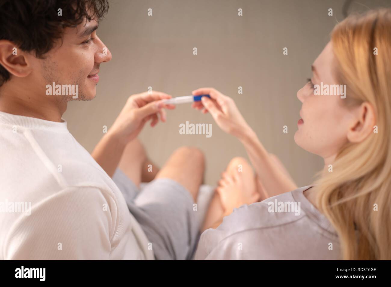 Coppia felice seduta sul letto e sorridente di eccitazione guardando un test di gravidanza positivo || modello rilasciato Foto Stock