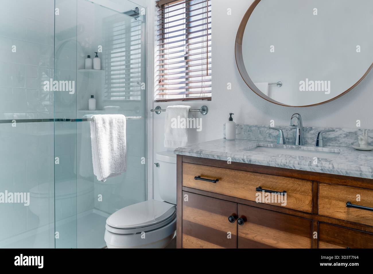 Bagno interno bianco moderno con lavandino in marmo, rubinetto, armadio in legno, doccia in vetro, specchio, e il bagno Foto Stock