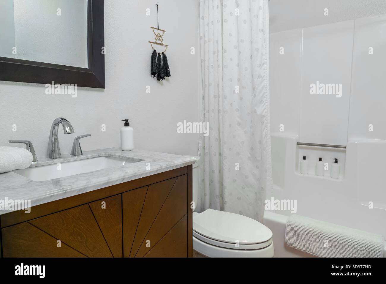 Bagno interno moderno e bianco con lavandino in marmo, rubinetto, armadio in legno e doccia con vasca Foto Stock