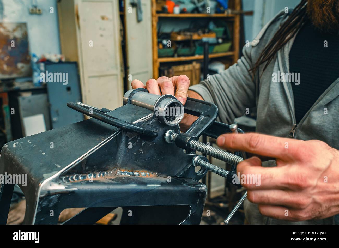 Le mani maschio stringono le parti metalliche insieme al morsetto. Il morsetto è dotato di una vite filettata per il serraggio e la regolazione della pressione. Informazioni generali sulle officine industriali. Foto Stock
