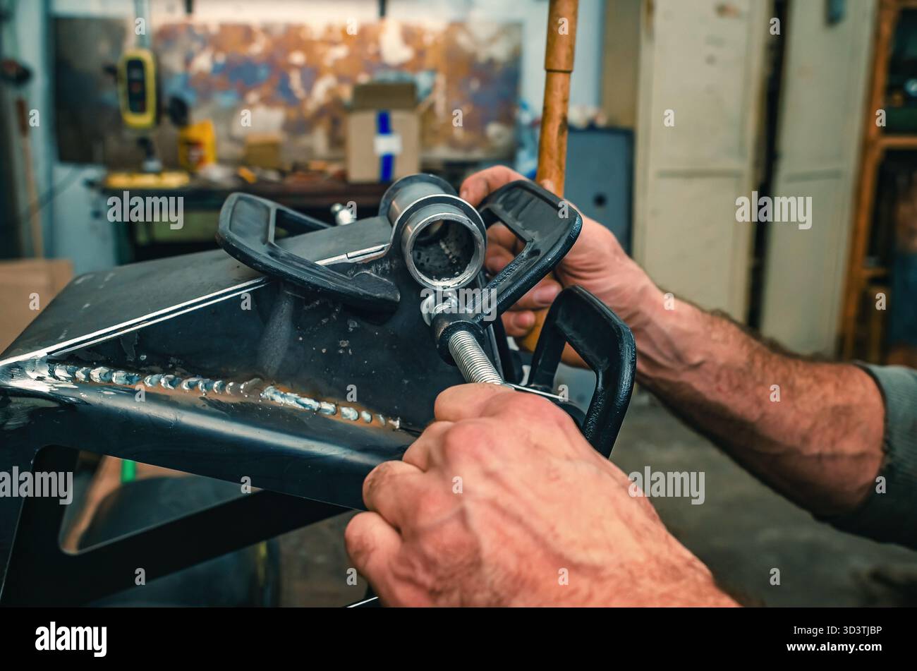 Le mani maschio stringono le parti metalliche insieme al morsetto. Il morsetto è dotato di una vite filettata per il serraggio e la regolazione della pressione. Informazioni generali sulle officine industriali. Foto Stock