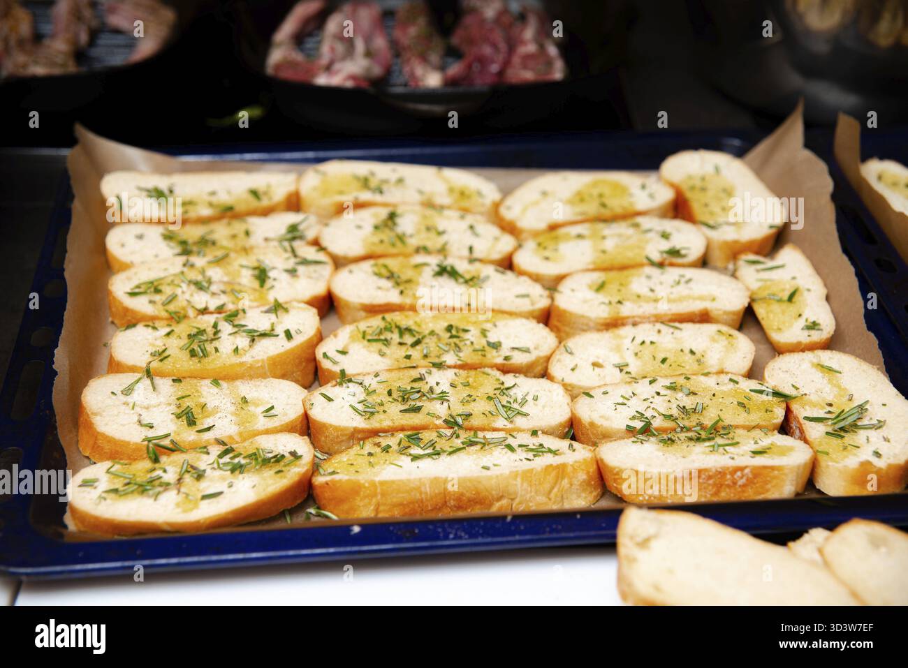 Cibo, fette fresche di baguette ricoperte di aglio, erbe aromatiche e olio d'oliva disposte su una teglia da forno, pronte per la tostatura Foto Stock
