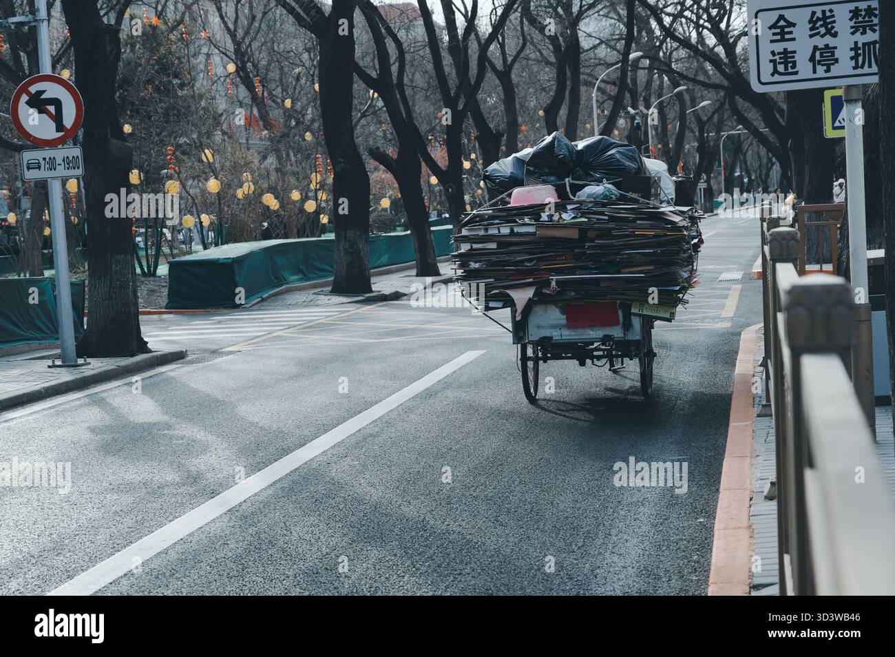 Il triciclo caricato con cartone impilato e materiali riciclabili si sposta lungo una strada alberata a Pechino Foto Stock