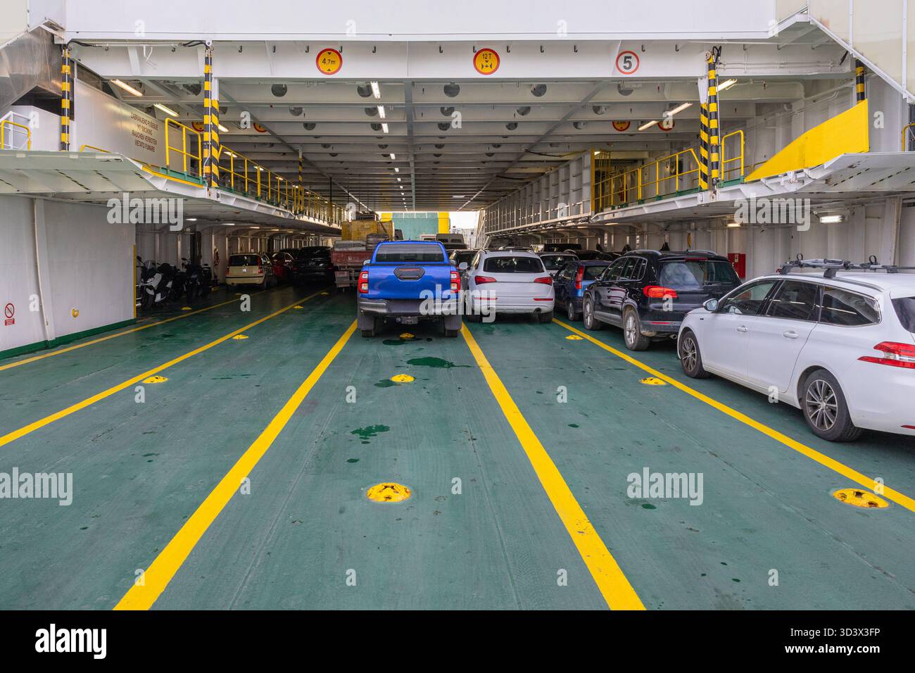 Le auto fermano un ponte del traghetto in un viaggio frenetico. Il pavimento verde, le marcature gialle e le auto parcheggiate creano una sce per viaggi industriali affollata Foto Stock