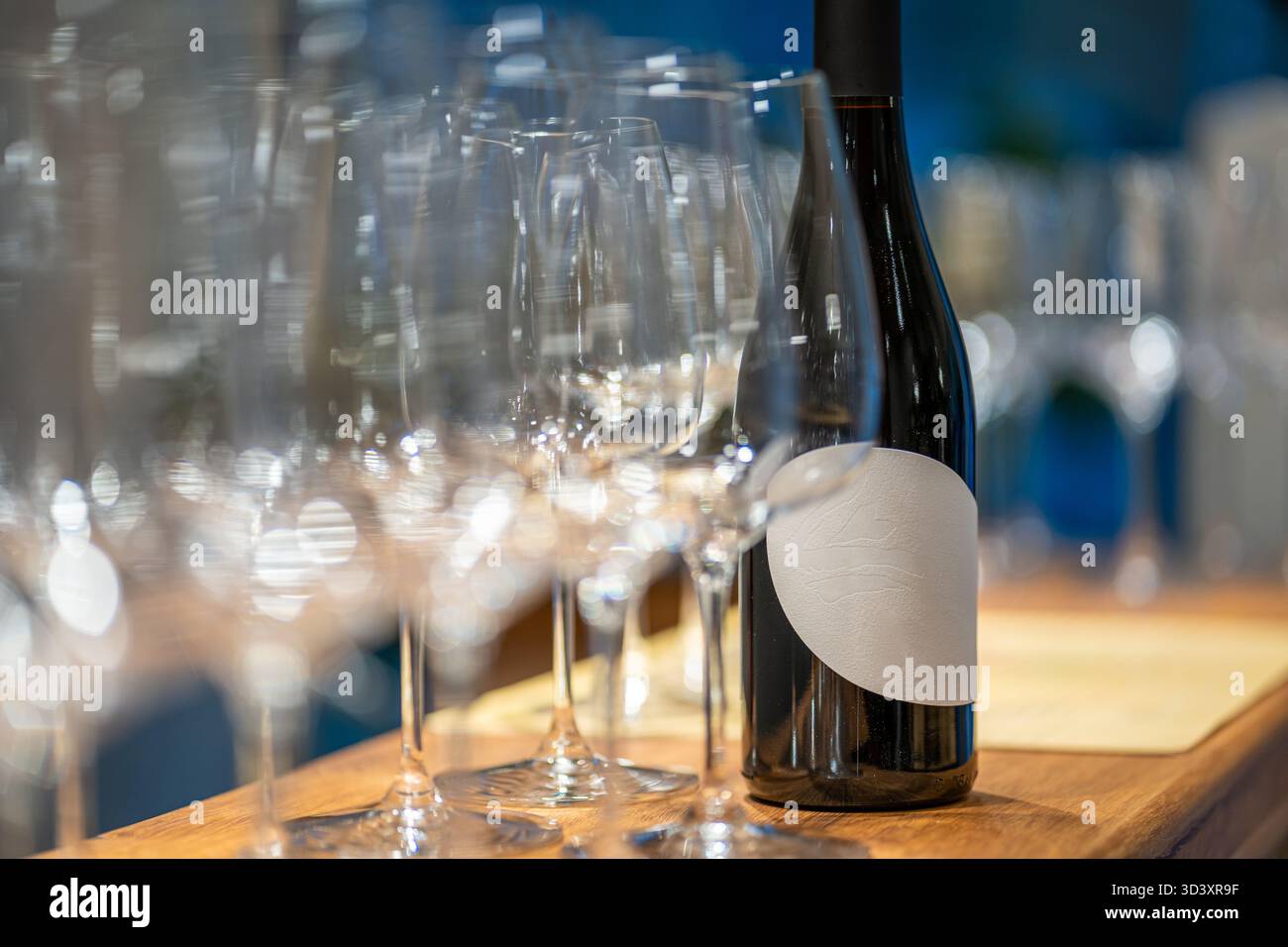 Bottiglia di vino con etichetta vuota in piedi su una barra di legno con molti bicchieri Foto Stock