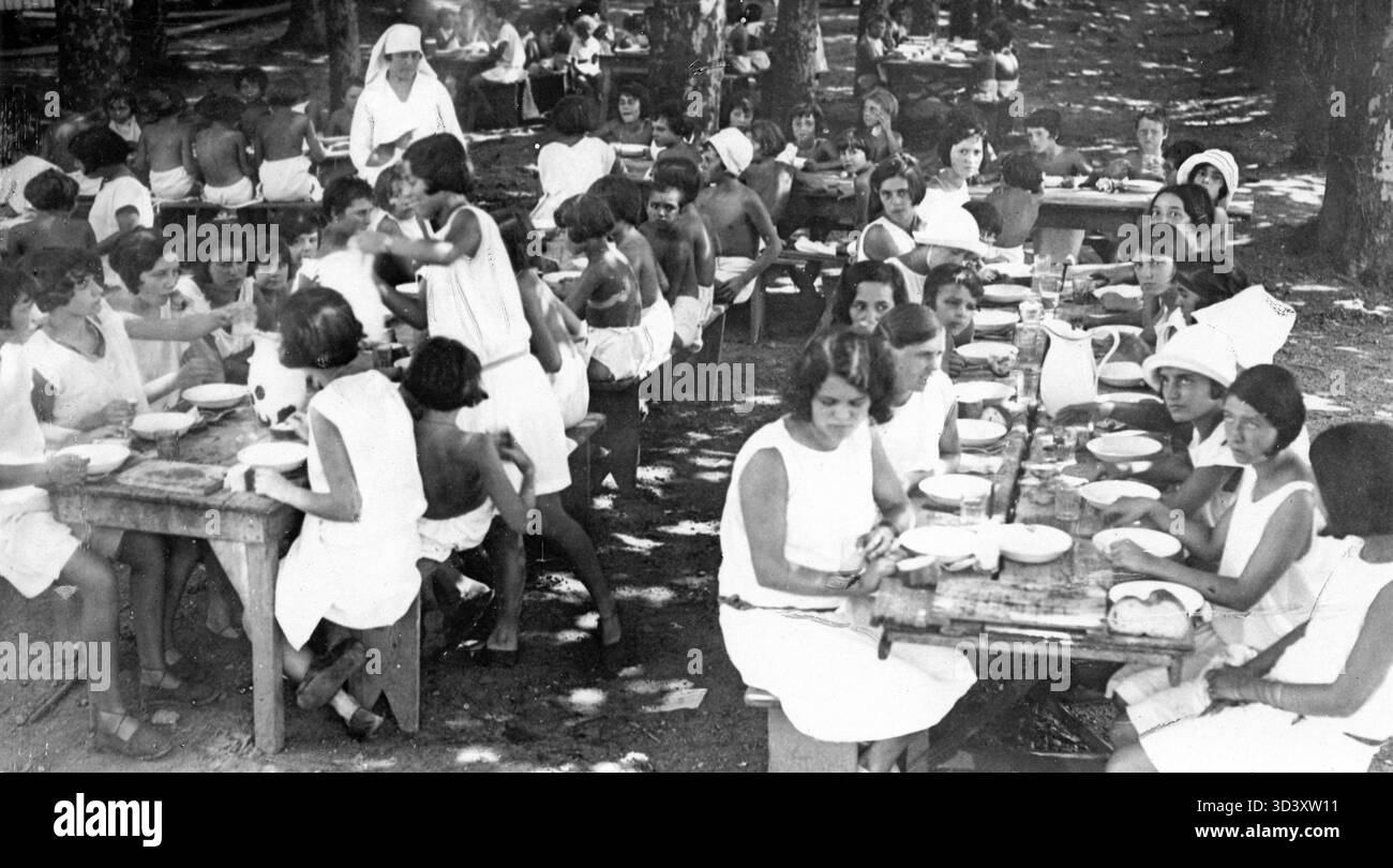 Donne e bambini mangiano fuori sotto la supervisione di una suora come parte degli sforzi di trattamento della tubercolosi in Francia, 1929. Foto Stock