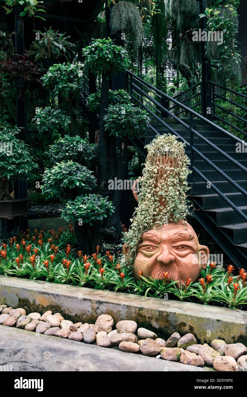 Una grande pianta verde con una faccia adagiata davanti a un muro. La pianta è circondata da rocce e fiori, creando un'atmosfera tranquilla e serena Foto Stock