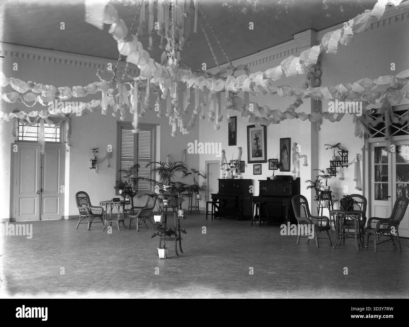 Vita coloniale in Indonesia (ex Indie Orientali olandesi) tra il 1895 e il 1910: Una sala decorata con due pianoforti, sedie, tavoli e pareti adornate con dipinti e fotografie, possibilmente in una scuola missionaria. Foto Stock