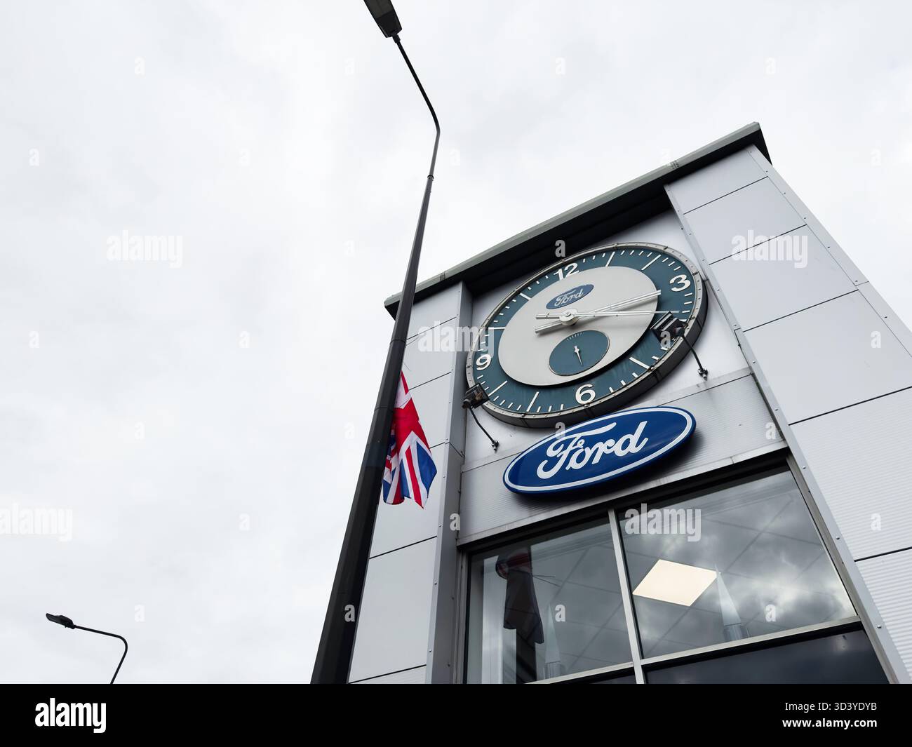 Manchester, Regno Unito - 30 settembre 2025: Orologio e marchio Ford su un elegante negozio di Manchester con bandiera e ambientazione urbana. Foto Stock