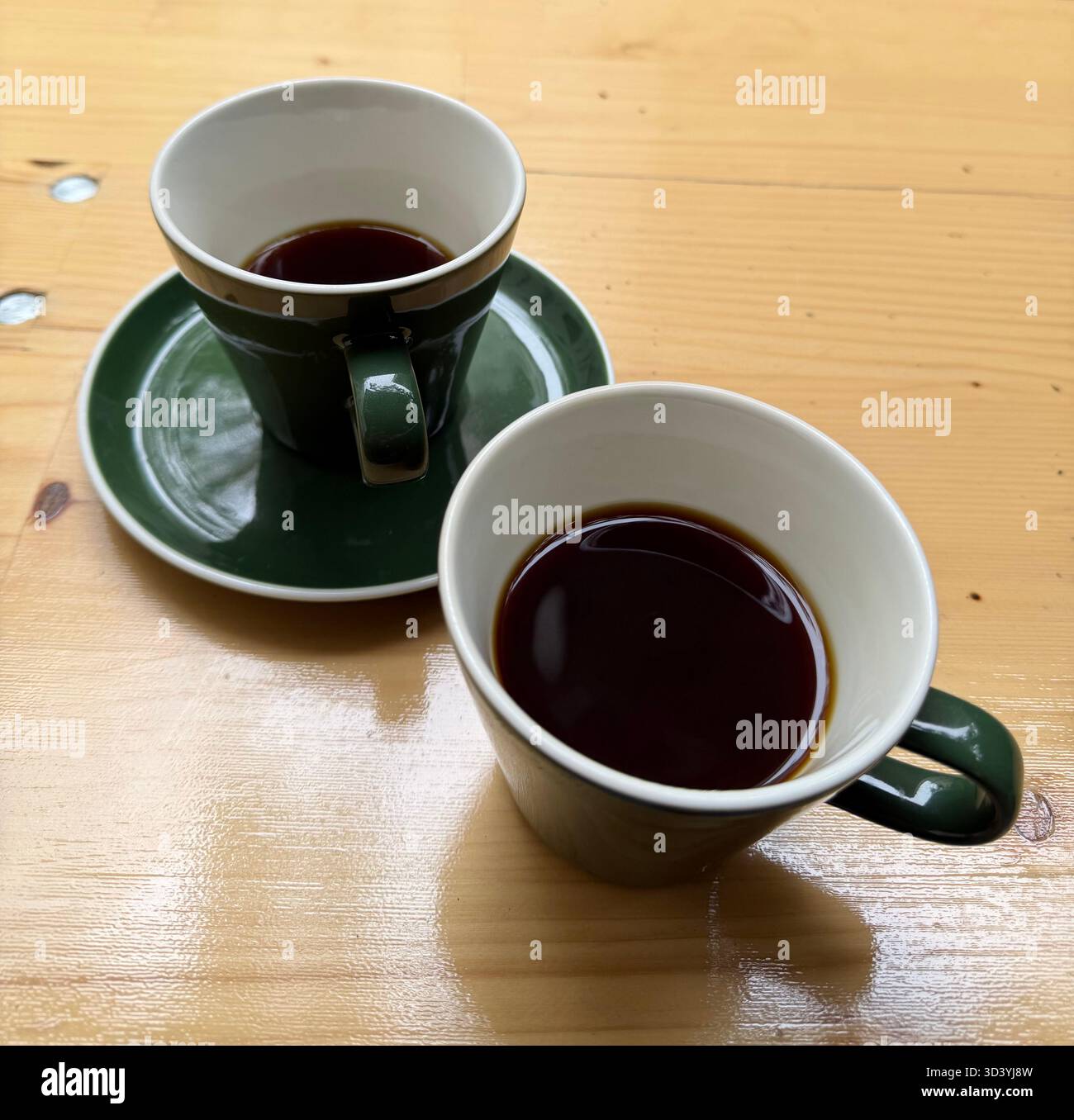 Due tazze di caffè nero in ceramica verde su un tavolo in legno verniciato, luce naturale, natura morta minima. - Immagine stock catturata con smartphone