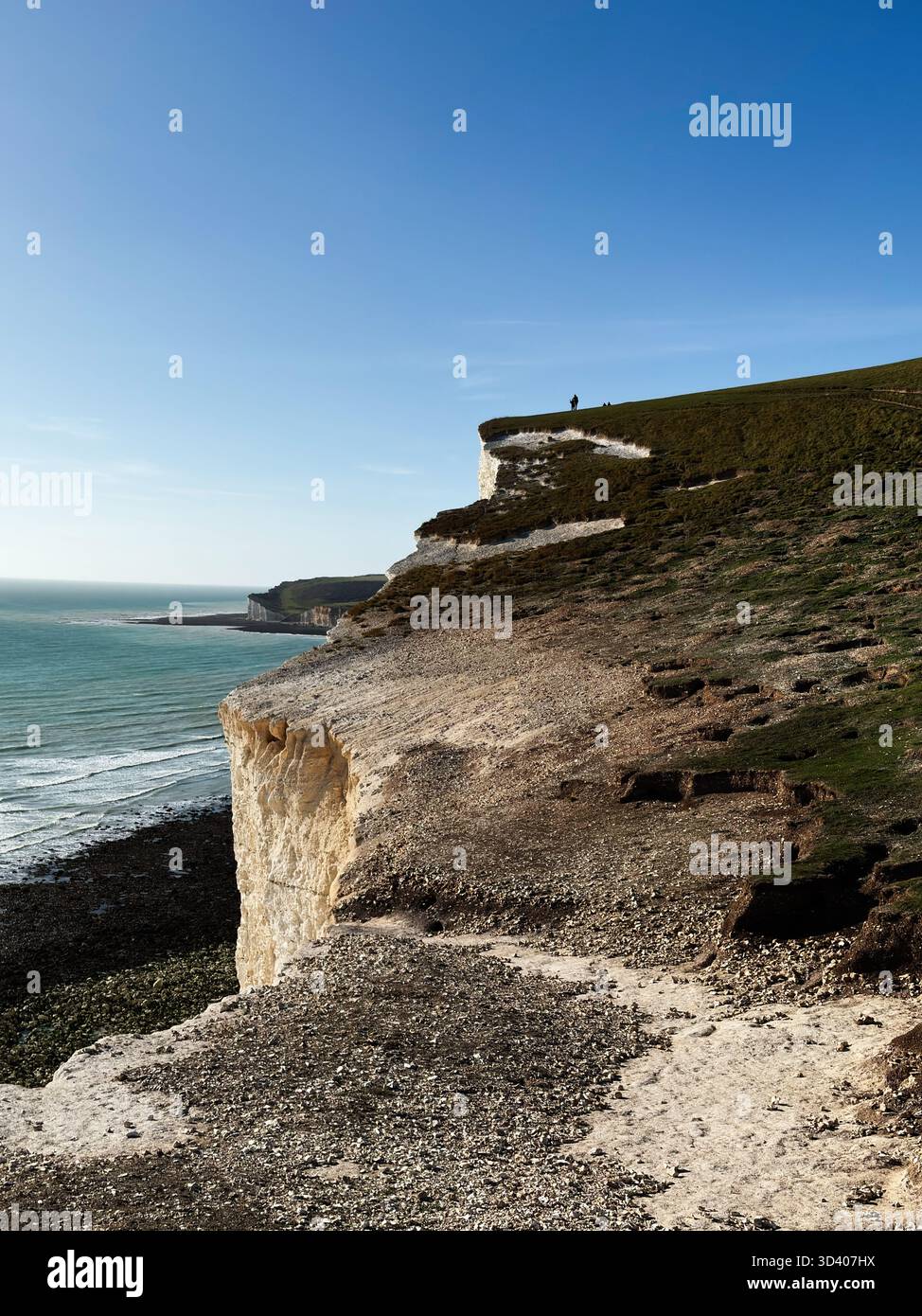 Scogliera costiera alle Seven Sisters Cliffs che mostra il mare blu, il sentiero di ciottoli e un lontano camminatore lungo il bordo. Foto Stock