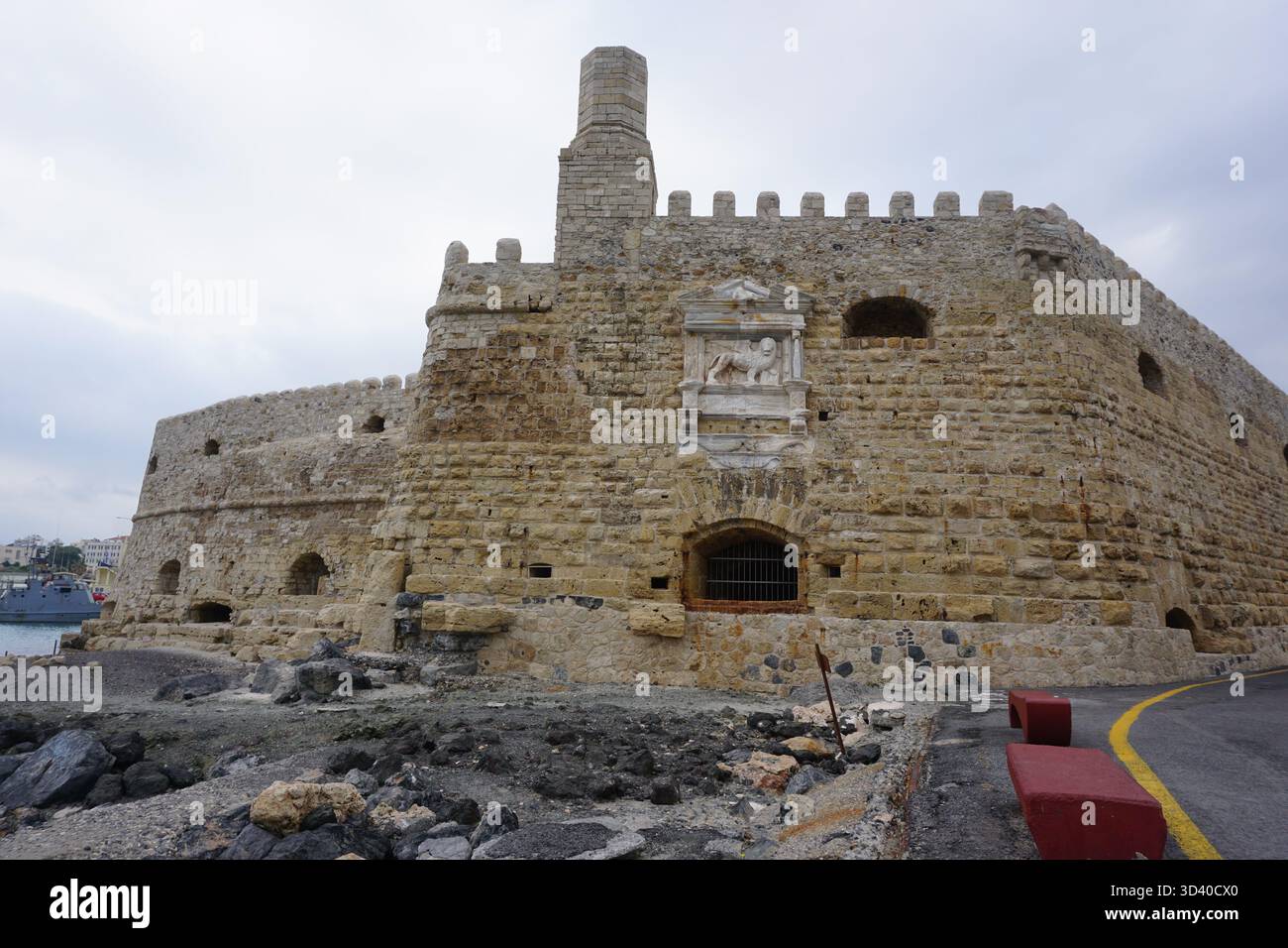 Vista d'angolo dell'imponente fortezza di Koules con la distinta torre di guardia simile a un camino e il rilievo del Leone di San Marco contro un cielo grigio. Foto Stock