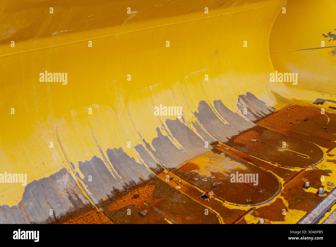 Superficie metallica gialla della benna dell'escavatore che mostra vernice raschiata, ruggine e usura strutturale che rappresenta l'uso di macchinari edili pesanti, equi Foto Stock