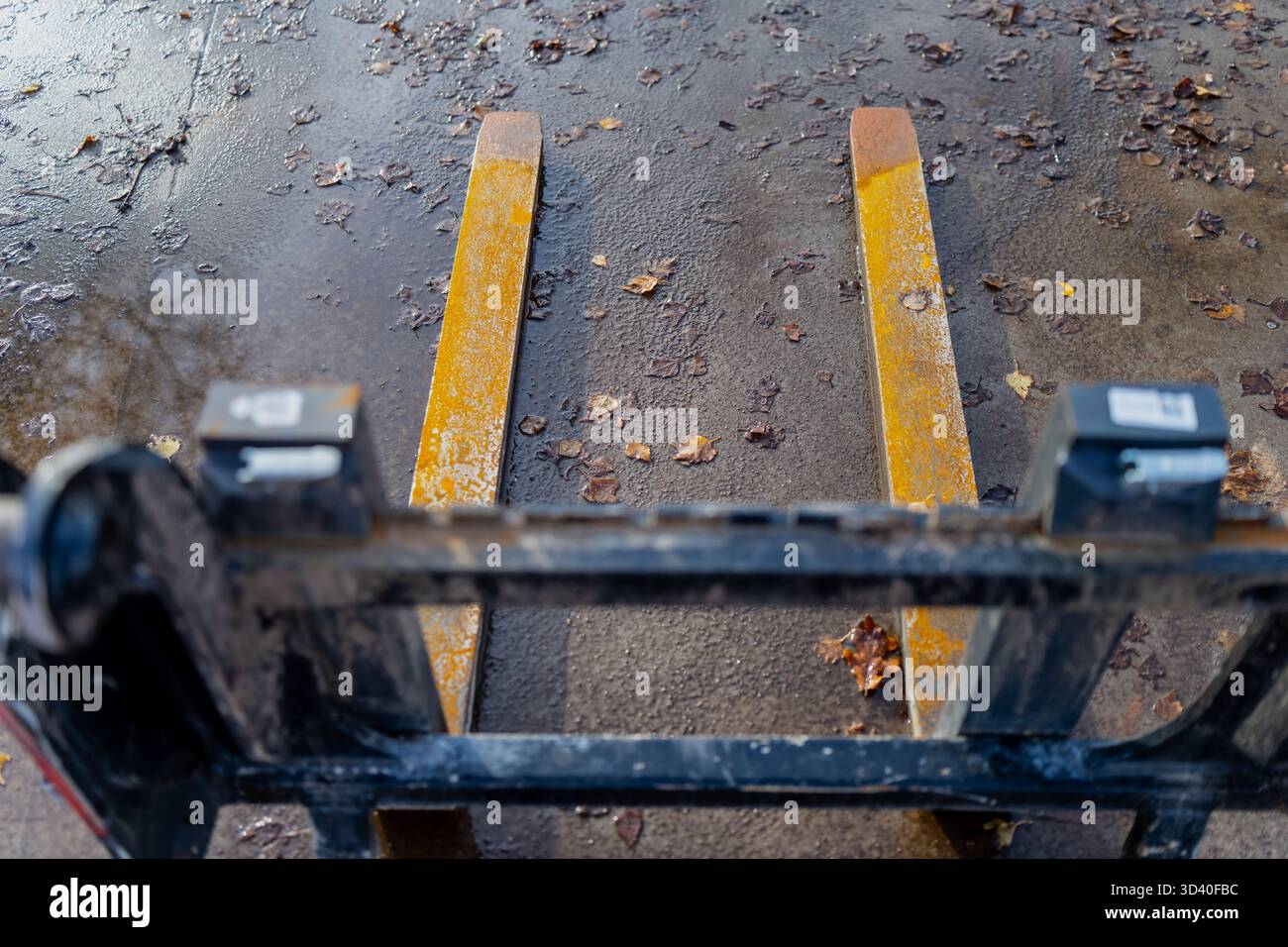 Forche gialle per carrelli elevatori su pavimentazione bagnata che rappresentano operazioni logistiche, movimentazione di costruzioni, processo di trasporto in magazzino e attrezzature pesanti utilizzate per Foto Stock