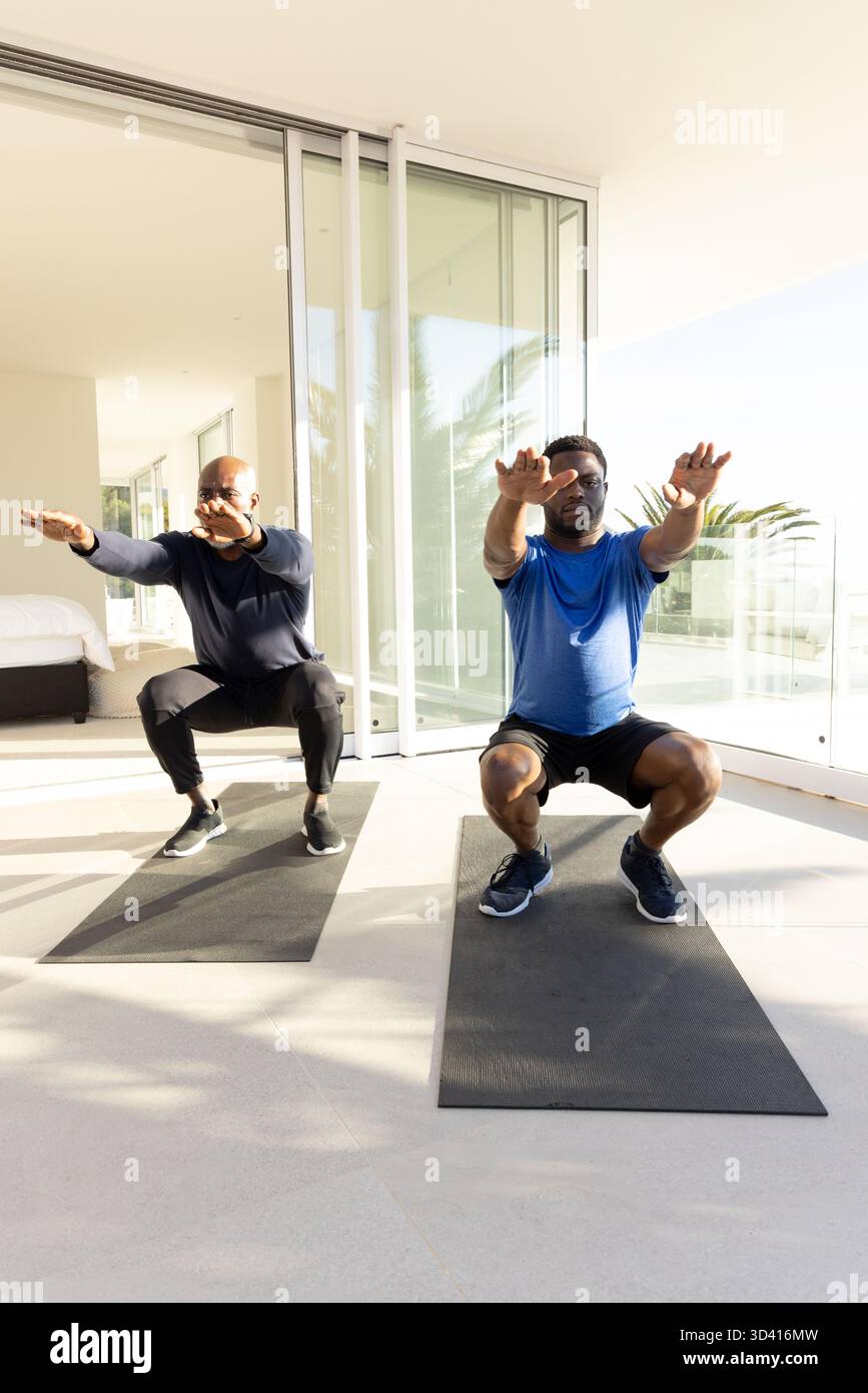 Padre e figlio afroamericani che si allenano sul balcone, con tappetini neri per yoga Foto Stock