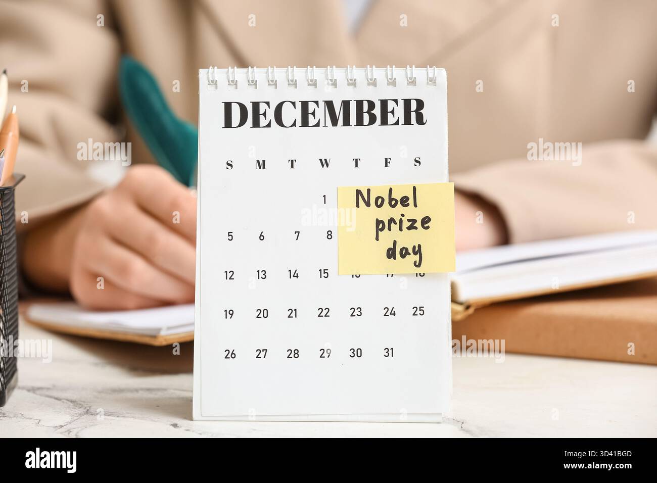 Calendario con testo GIORNATA DEL PREMIO NOBEL contro la donna che scrive nel libro su tavola, primo piano. Giorno del premio Nobel Foto Stock