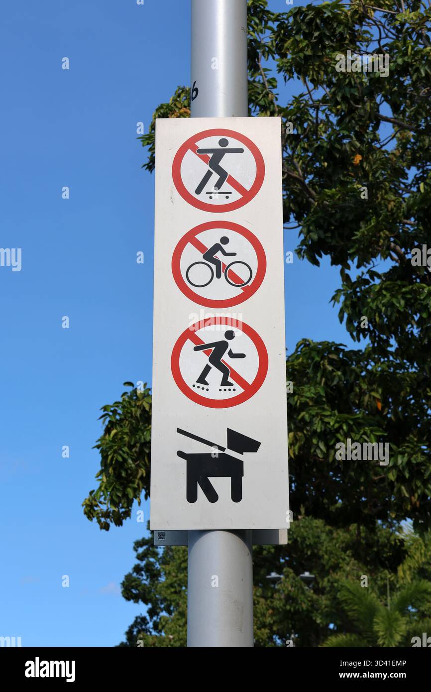 Insegna che proibisce skateboard, ciclisti e lame a rulli, ma consente ai cani di indossare guinzagli attaccati a un palo metallico in un parco Foto Stock