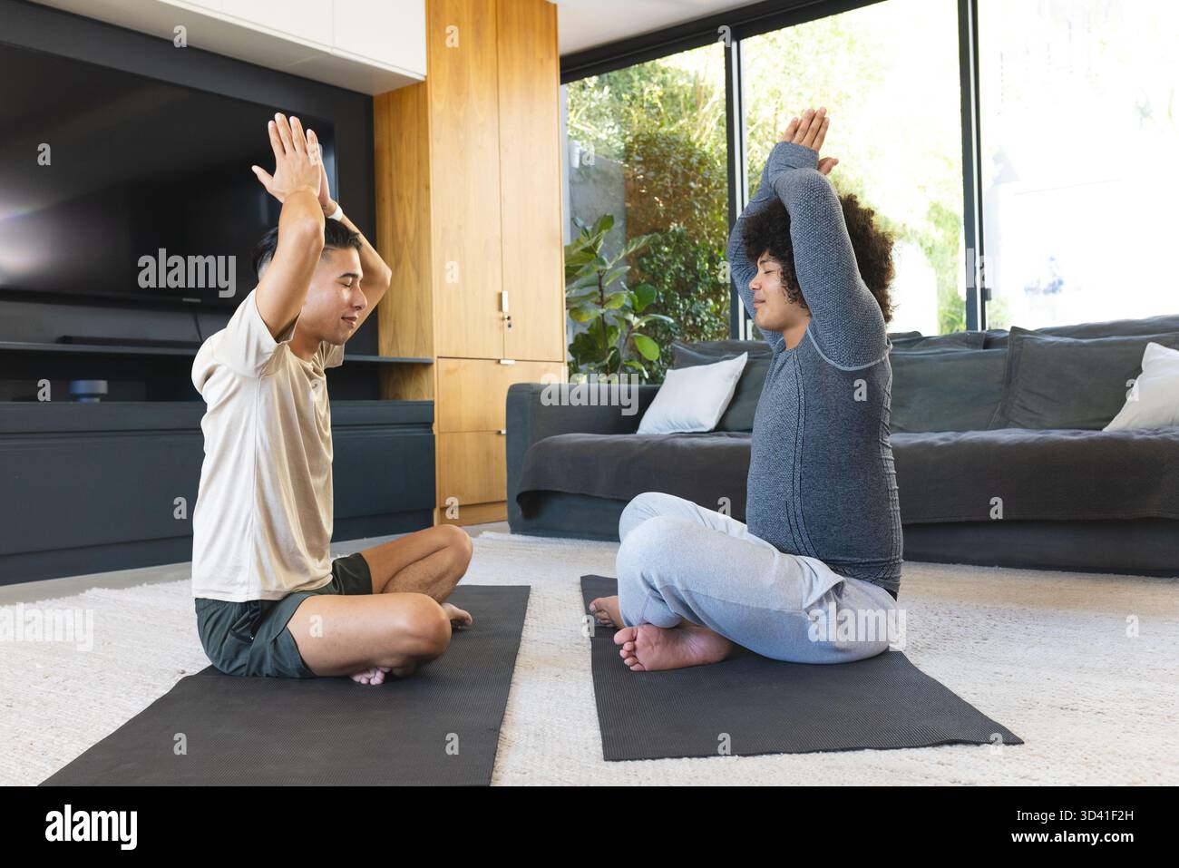 Distendete diversi amici maschi che praticano yoga nel soggiorno, con tappeti neri e grandi finestre Foto Stock