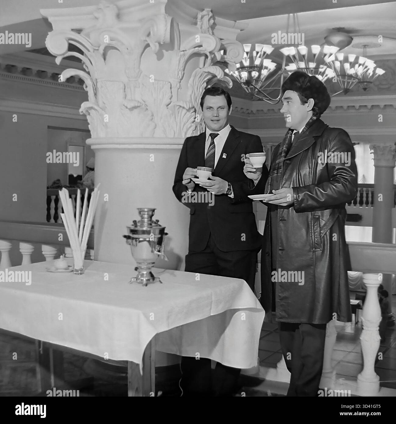 Una foto d'archivio del 1984 mostra due delegati maschi in una conferenza nella Casa della Cultura Artyom (DK) a Sloviansk, RSS Ucraina. Gli uomini sono in pausa tè, in piedi accanto a un tavolo con un samovar tradizionale. Si trovano nel grande atrio, riconoscibile per le sue colonne ornate e i lampadari. L'uomo sulla destra indossa un caratteristico cappello di pelliccia (ushanka), suggerendo che è freddo. Questo cattura un momento di discussione durante un evento ufficiale sovietico. Questo mostra la vita quotidiana nel pacifico Donbas prima della guerra. Foto Stock