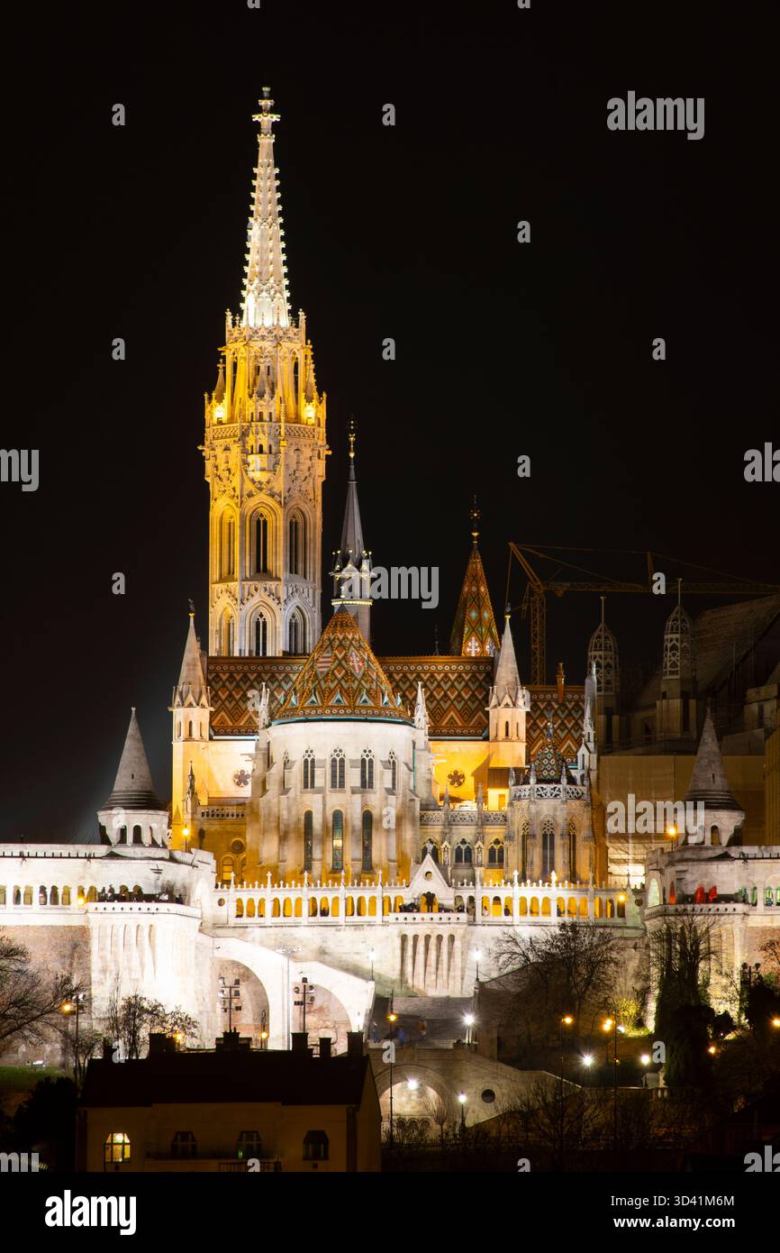 Primo piano della torre illuminata della chiesa di Mattia con dettagli neogotici che brillano contro il cielo scuro di Budapest. Foto Stock
